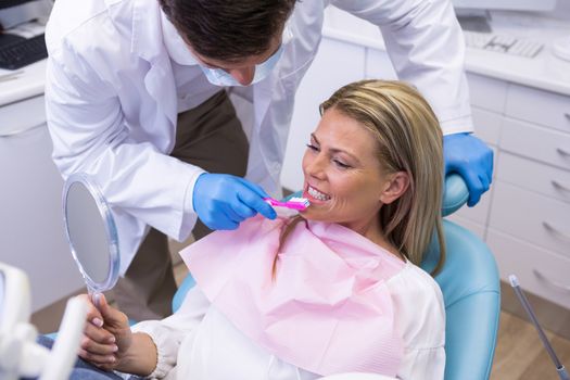 Dentist assisting woman in brushing teeth at dental clinic