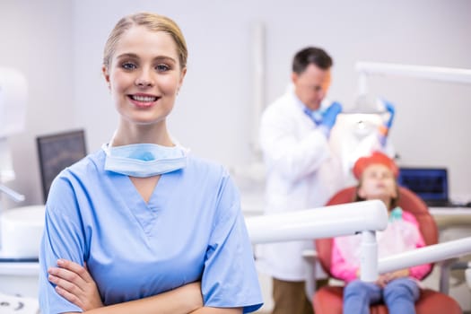 Portrait of smiling nurse with arms crossed while dentist examining patient in background