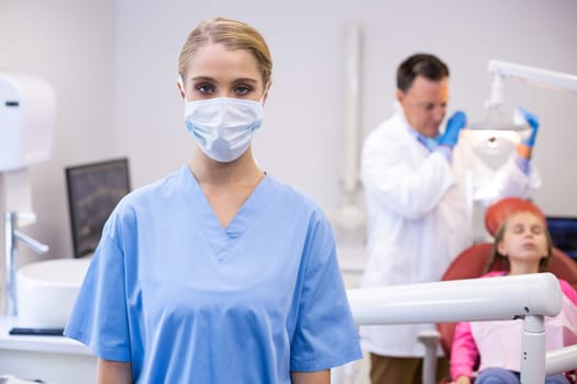 Portrait of female nurse wearing surgical mask while dentist examining patient in background