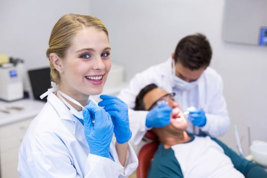 Dentist holding dental tool while his colleague examining patient in background at clinic