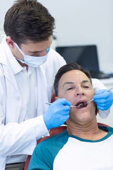 Dentist examining a male patient with tools in clinic