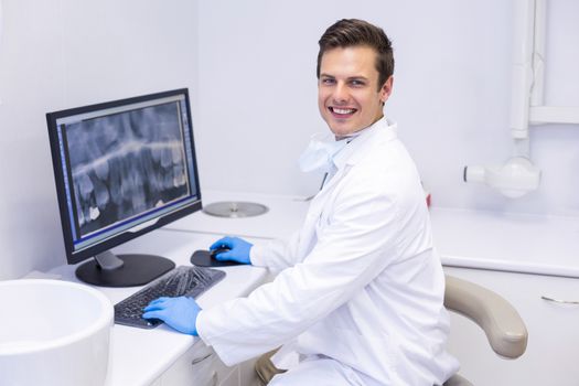 Portrait of happy dentist examining x-ray report on computer in clinic