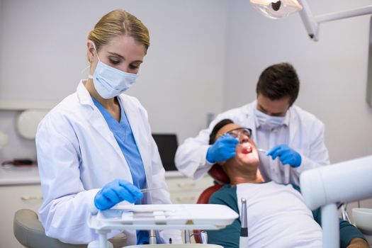 Dentist holding dental tool while his colleague examining patient in background at clinic