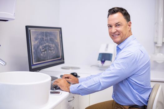 Portrait of happy dentist examining x-ray report on computer in clinic