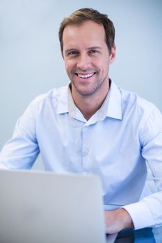 Portrait of smiling dentist working on laptop in dental clinic