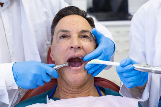 Dentist examining a male patient with tools in clinic