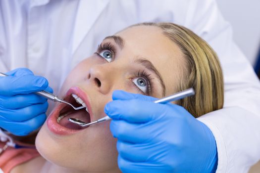 Dentist examining a female patient with tools at clinic