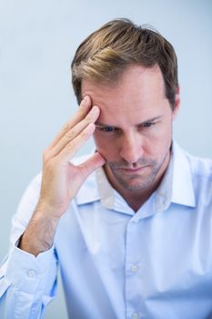 Close-up of tensed dentist sitting with hand on forehead in clinic