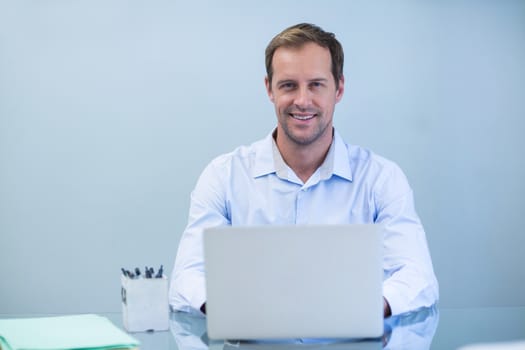 Portrait of smiling dentist working on laptop in dental clinic