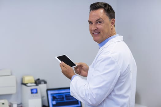 Portrait of smiling dentist holding digital tablet in dental clinic