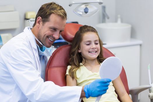 Smiling dentist showing mirror to young patient in dental clinic