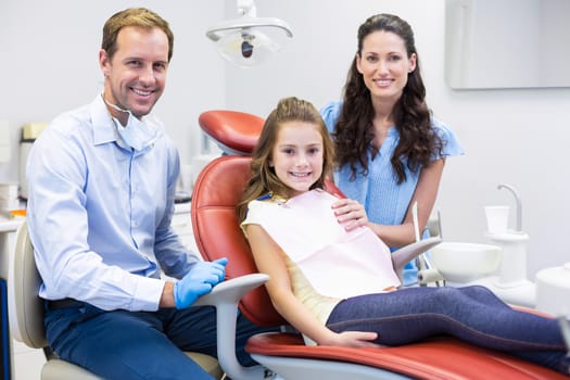 Portrait of dentist with young patient and her mother at dental clinic