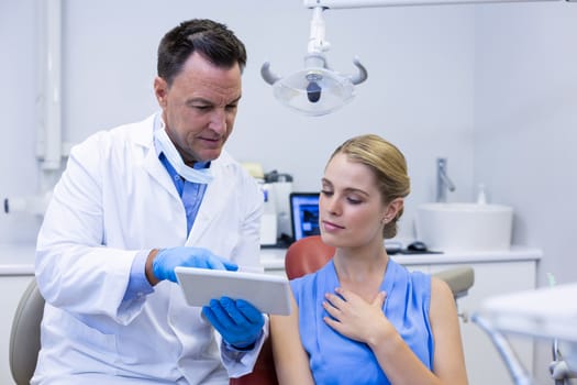 Dentist discussing over digital tablet with female patient in dental clinic