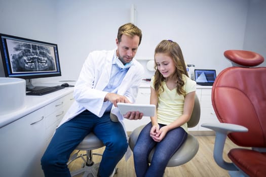 Dentist showing digital tablet to young patient in dental clinic