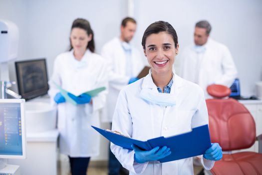 Portrait of smiling dentist holding file at dental clinic