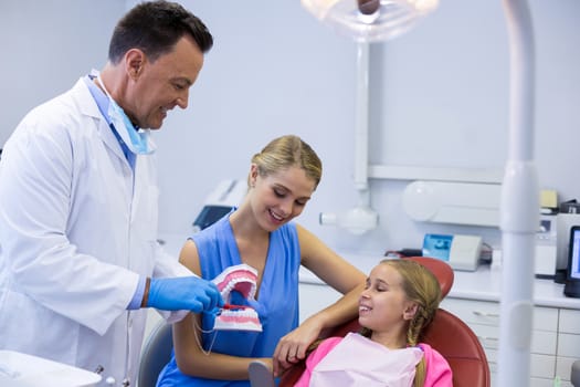 Dentist showing young patient how to brush teeth in dental clinic