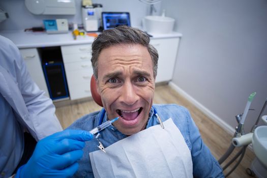 Dentist injecting anesthetics in scared male patient mouth at dental clinic