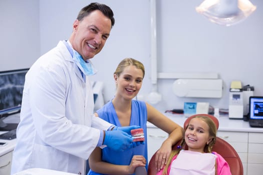 Portrait of dentist showing young patient how to brush teeth in dental clinic