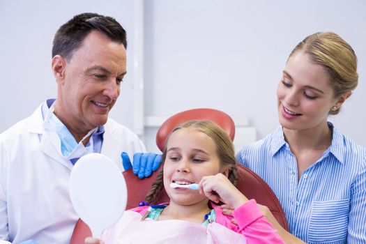 Dentist assisting young patient while brushing teeth in dental clinic