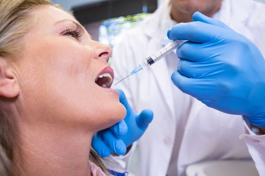 Close up of dentist holding syringe by patient at medical clinic