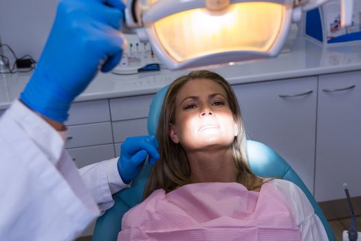 Woman lying on dentist chair while dentist adjusting electric lamp at clinic