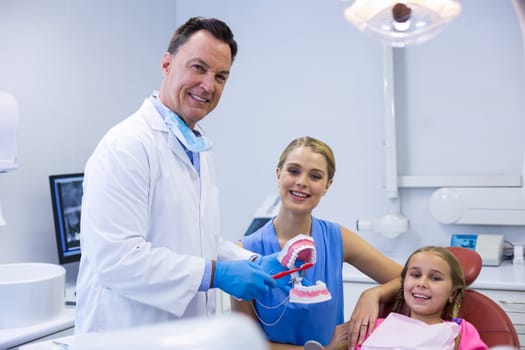 Dentist showing young patient how to brush teeth in dental clinic