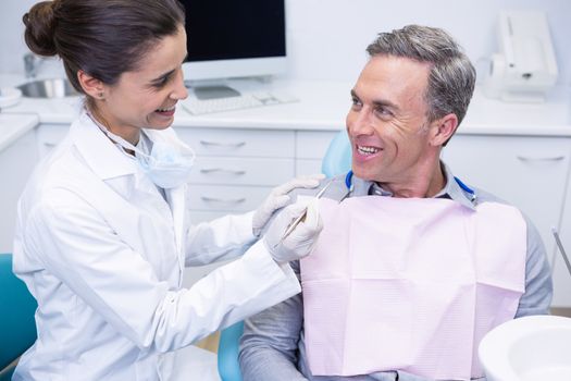 Happy dentist holding tool while looking at man in medical clinic