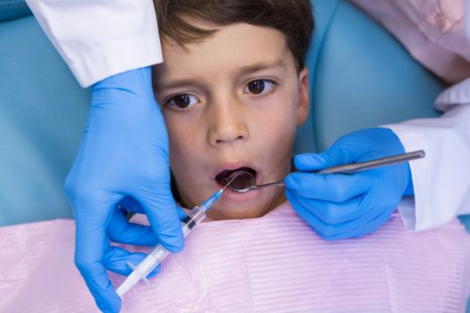 High angle view of dentist holding syringe while treating boy at medical clinic