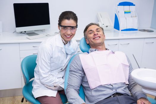 Portrait of smiling dentist and patient sitting on chair at medical clinic
