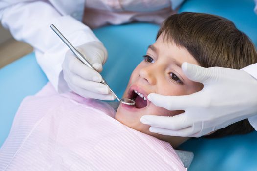 Cropped image of dentist holding equipment while examining boy at medical clinic