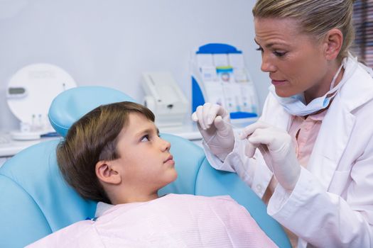 Dentist holding medical equipment while talking to boy at clinic