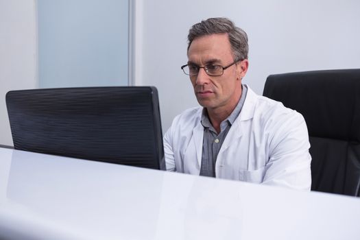 Dentist sitting by computer at table in clinic