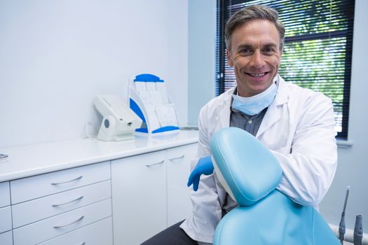 Portrait of smiling dentist standing by chair at medical clinic