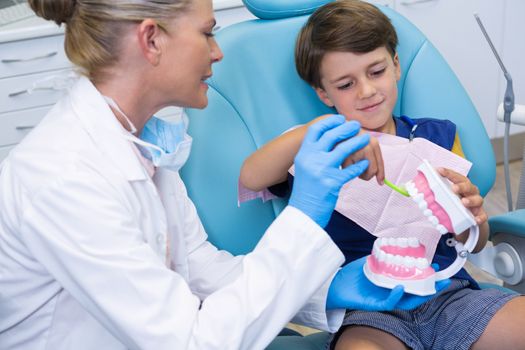 Dentist looking at boy brushing dentures at clinic