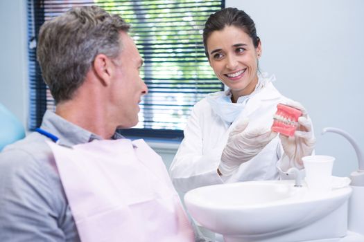 Happy dentist showing dental mold to man at clinic