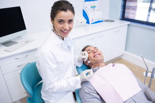 Portrait of dentist holding equipment while standing by patient at medical clinic