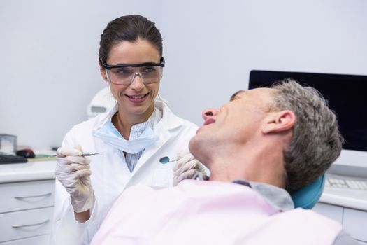 Happy dentist holding tool while looking at man in clinic