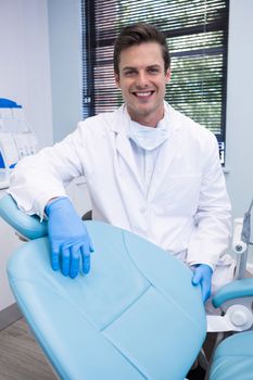 Portrait of dentist standing by chair against window at clinic