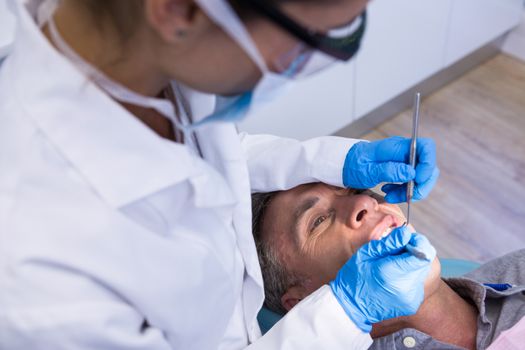 High angle view of dentist holding tools while examining man at clinic