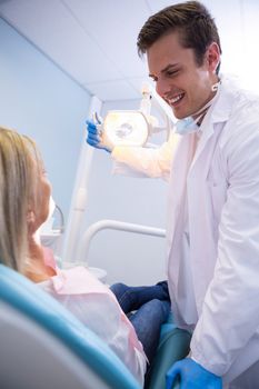 Low angle view of dentist adjusting lamp while looking at patient in clinic
