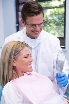 Dentist showing mirror to smiling patient at dental clinic