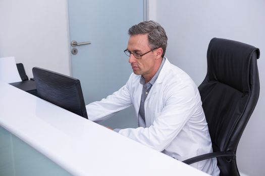 High angle view of dentist sitting by computer at table in clinic