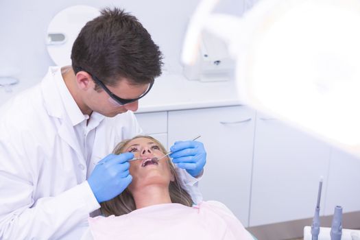 High angle view of dentist holding equipment while examining woman at medical clinic