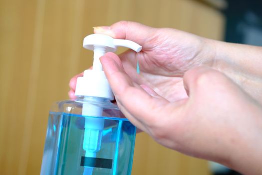 Female Hand dispensing blue liquid soap or cleanser gel from glass container. Washing hands, hygiene and healthy life concept. Close up, selective focus. Finger pushing the soap dispenser. 