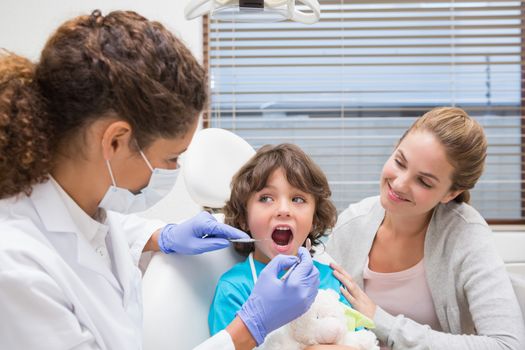 Pediatric dentist examining a little boys teeth with his mother at the dental clinic