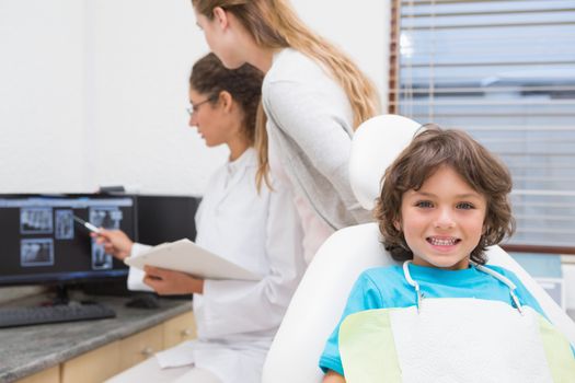 Little boy smiling at camera with mother and dentist in background at the dental clinic