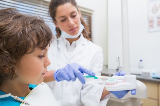 Pediatric dentist showing little boy how to brush his teeth at the dental clinic