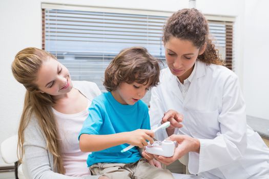 Pediatric dentist showing little boy how to brush teeth with his mother at the dental clinic