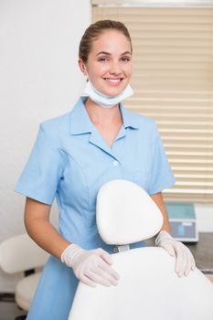 Dental assistant smiling at camera beside chair at the dental clinic