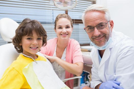 Little boy smiling at camera with mother and dentist beside him at the dental clinic